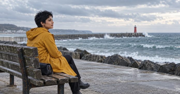 Woman in a yellow coat sitting quietly beside the sea